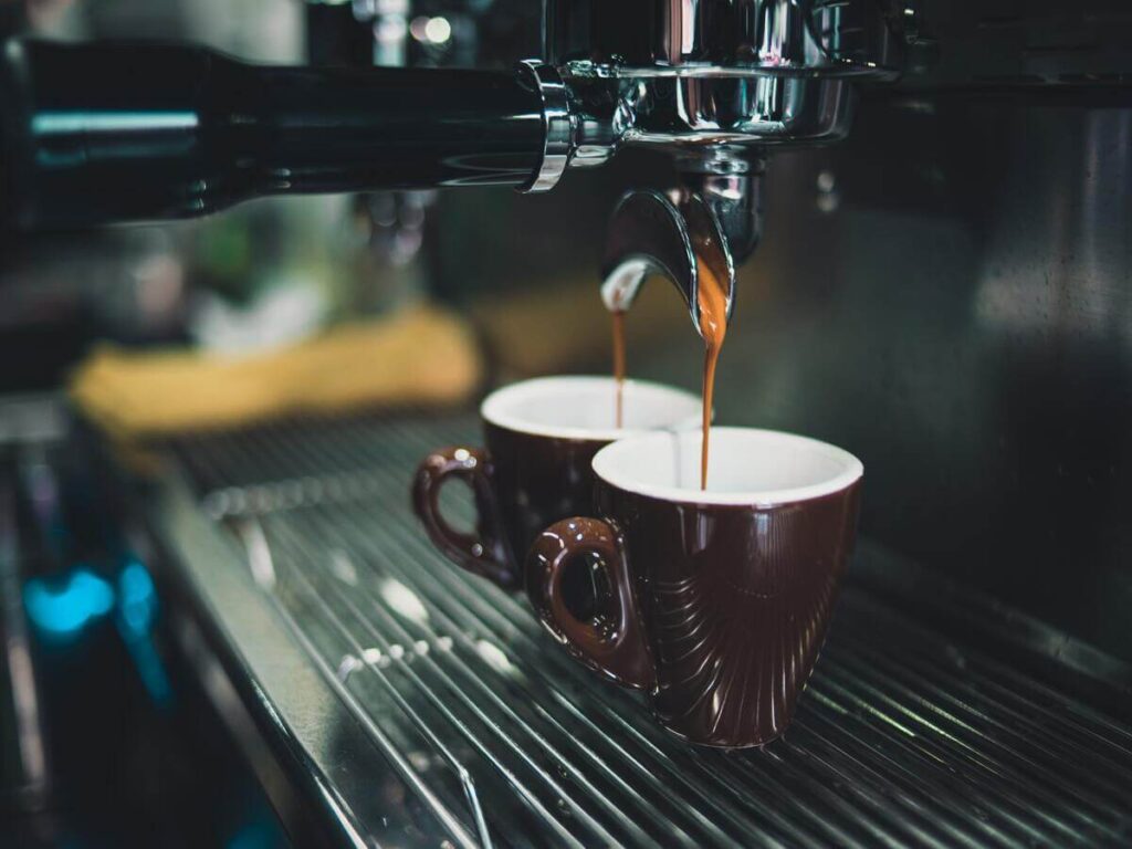 Pulizia Macchina da Caffé; nell'immagine una macchina da caffè da bar professionale in azione mentre eroga caffè in due tazzine colore scuro