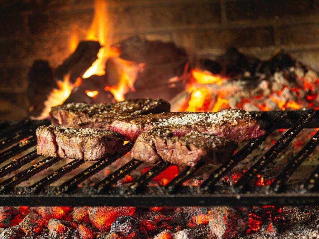 Come pulire il barbecue; l'immagine mostra una griglia con un bel fuoco sotto e della buonissima carne in cottura