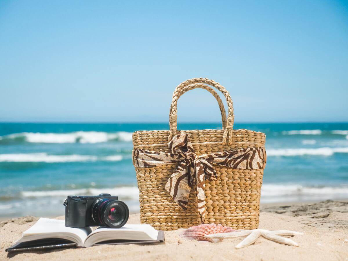 In questa foto vediamo una borsa per la spiaggia con un libro e una macchina fotografica 
