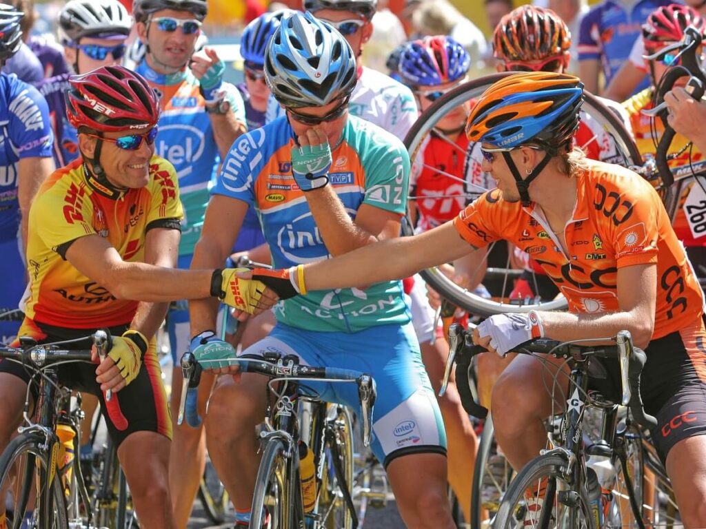 La foto rappresenta la partenza di una gara ciclistica con una serie di atleti con completi variopinti, biciclette super professionali e una serie dei migliori caschi per bici da corsa