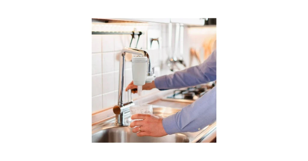 Acqua filtrata 2026: come avere acqua buona in casa risparmiando sulle bottiglie Acqua filtrata 2026; Una persona in cucina riempie un bicchiere d'acqua filtrata pura da un depuratore xWater installato sul rubinetto cromato."