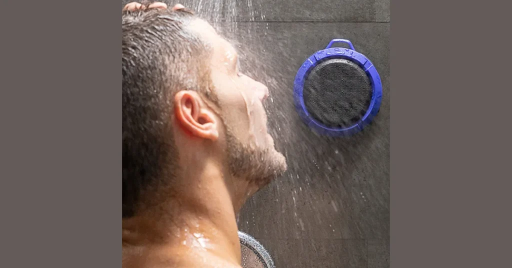 Cassa Bluetooth Doccia 2026: La Rivoluzione Audio Impermeabile per il Tuo Bagno Uomo sotto la doccia con cassa bluetooth 2026 blu attaccata alla parete resistente al getto d'acqua diretto.